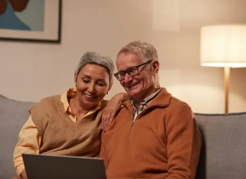 couple smiling together on sofa on online therapy session using laptop