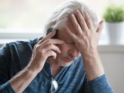 man on phone with hand on forehead looking in pain