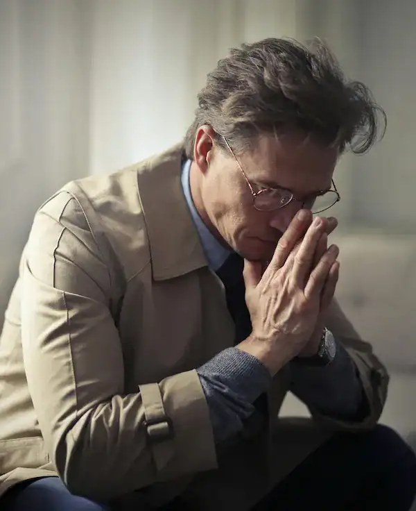man sitting on sofa looking down with hands in prayer position over nose