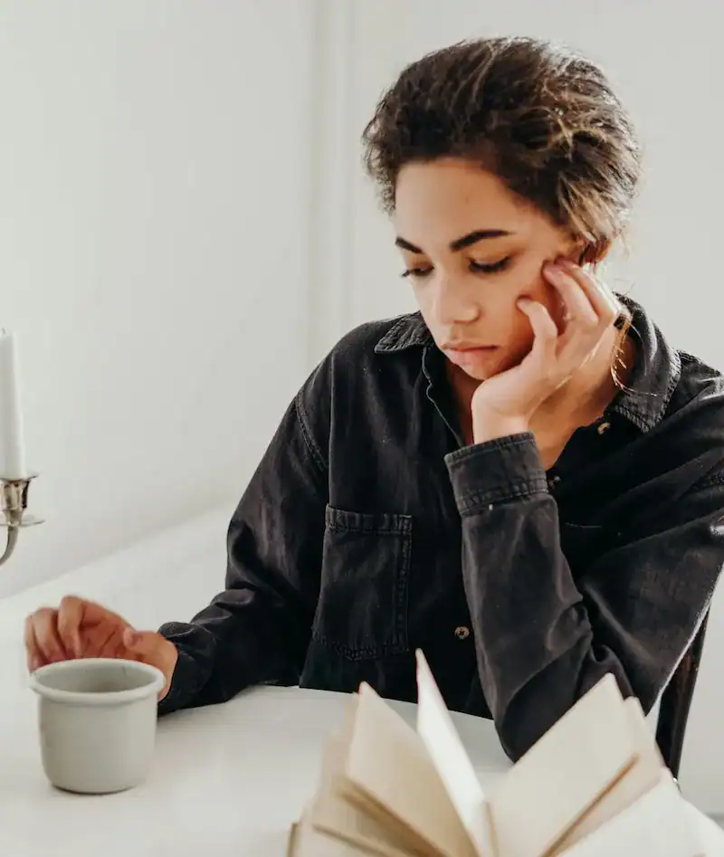 woman drinking coffee with book looking sad